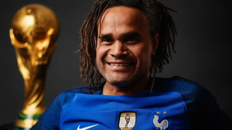 Christian Karembeu : son parcours incroyable en Coupe du Monde Christian Karembeu en maillot de l'équipe de France, souriant, avec le trophée de la Coupe du Monde 1998 dans les mains, sur fond de Stade de France.
