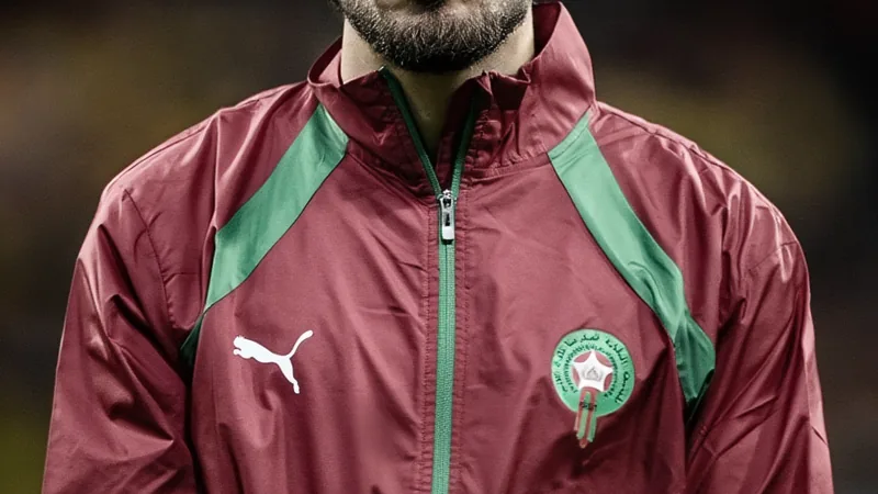 Joueurs marocains Ez Abde et Nayef Aguerd en tenue d'entraînement, tristes, avec un fond de terrain de football et le drapeau du Maroc