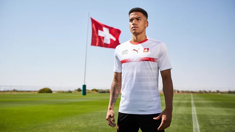 Ricardo Rodriguez en tenue d'entraînement de l'équipe de Suisse, souriant et tenant une lettre, sur un fond de terrain de football.