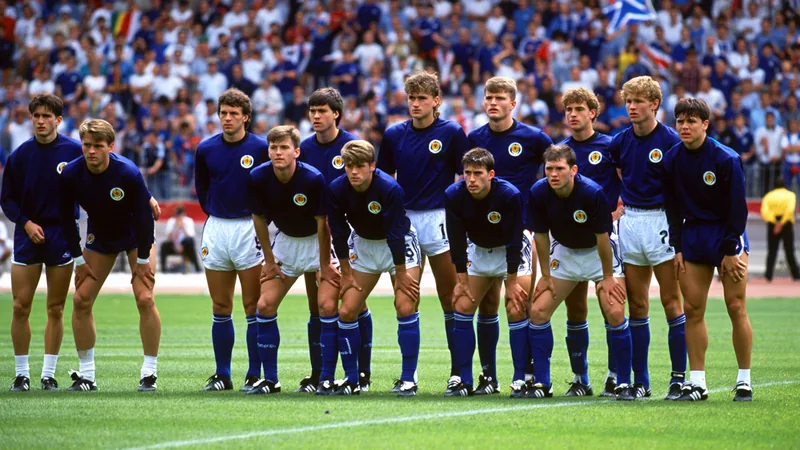 « Encore une histoire de malchance » – L’Écosse à la Coupe du monde Joueurs écossais en maillot bleu foncé quittant le terrain, tête baissée, sous les regards déçus des supporters du Tartan Army dans un stade italien.