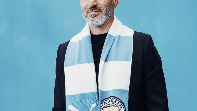 Enzo Maresca en costume, souriant lors d'une conférence de presse, avec le logo de Manchester City en arrière-plan. — latest news and analysis.