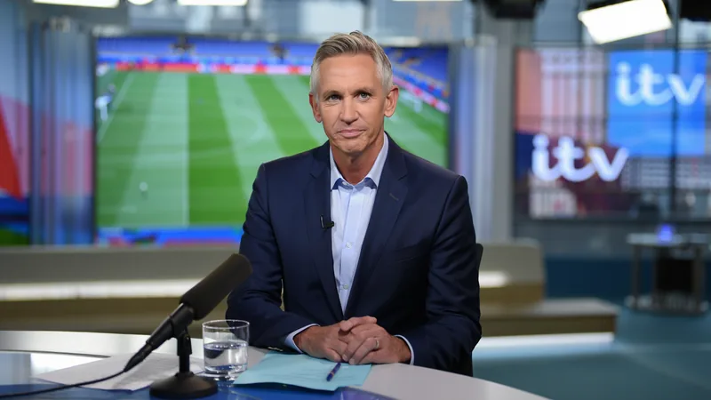 Gary Lineker en costume, souriant, assis dans un studio de télévision avec un micro-cravate, prêt à commenter un match de football.