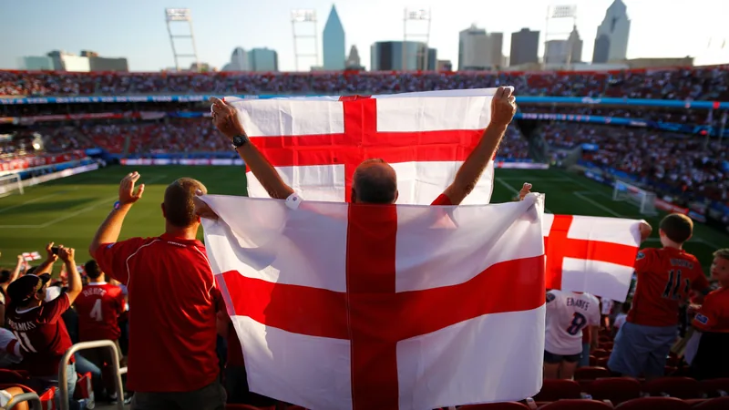 Jusqu'à 15 000 supporters anglais attendus à Dallas pour le Mondial Foule de supporters anglais agitant des drapeaux de saint Georges devant le Dallas Stadium, avec l'emblème de la Coupe du monde 2026 en arrière-plan.