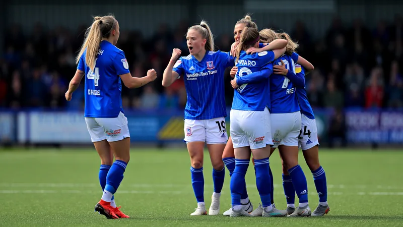 Kit Graham, attaquante d'Ipswich Town Women, célébrant un but lors d'un match de WSL 2, portant le maillot bleu et blanc, devant des supporters en