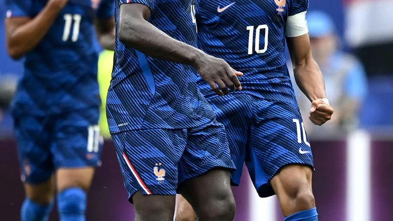 Kylian Mbappé célébrant un but avec l'équipe de France, portant le maillot bleu, devant un stade rempli de supporters français en liesse.