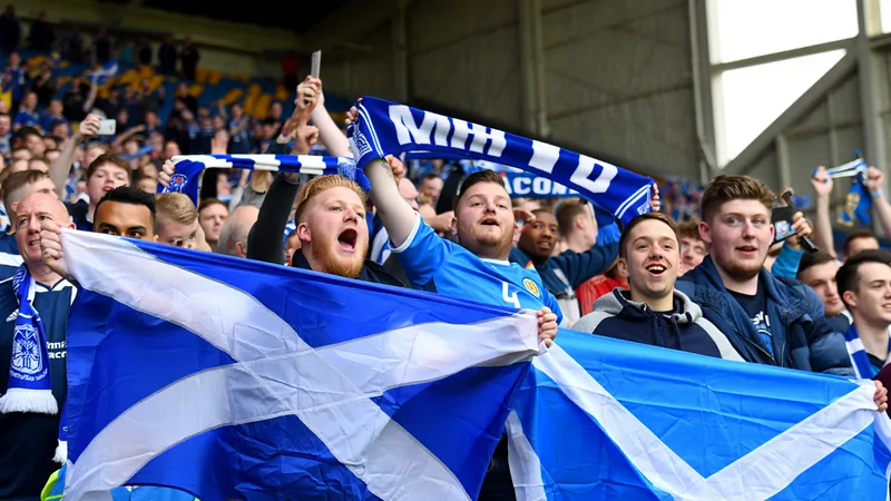 Supporters écossais en kilt agitant des drapeaux dans une fan zone à Édimbourg devant un écran géant affichant le match Écosse-Haïti