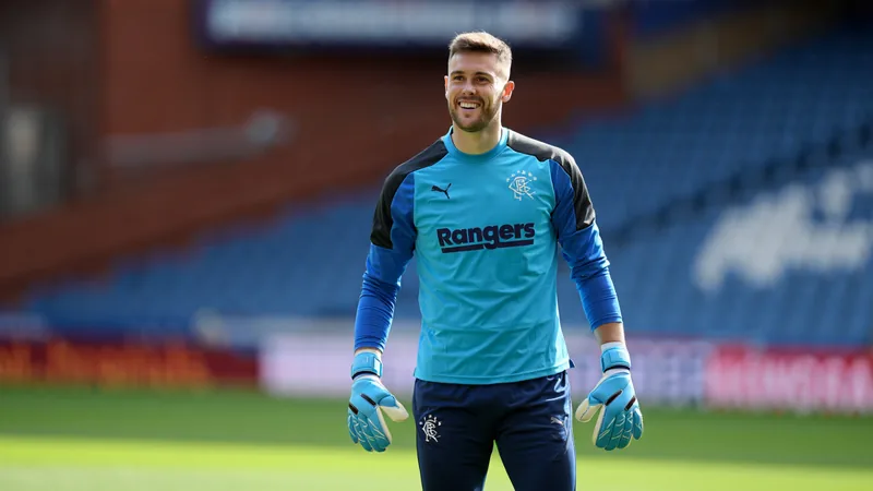 Liam Kelly en tenue des Rangers, souriant, avec le logo du club en arrière-plan et le stade d'Ibrox visible — latest news and analysis.