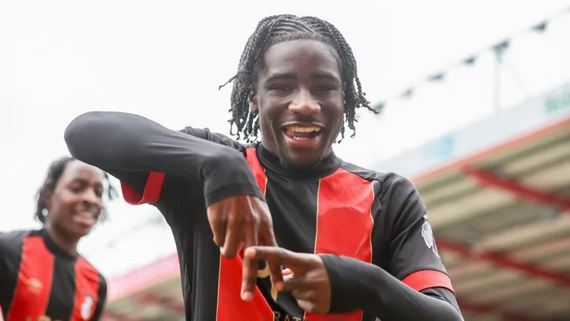 Un jeune joueur de football noir en tenue de Bournemouth, souriant, posant avec un maillot de Moreirense devant le logo du club.