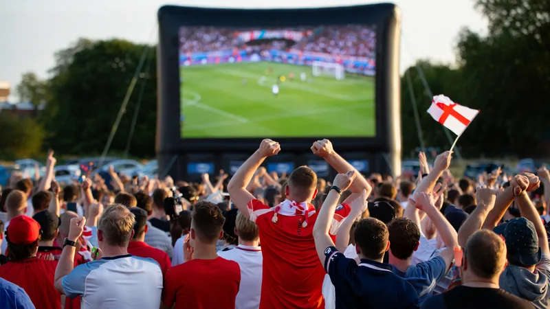 Où regarder les matchs de l'Angleterre dans le Sussex — Football Un pub bondé dans le Sussex avec un grand écran diffusant un match de l'Angleterre, des supporters en maillot blanc brandissant des drapeaux anglais.