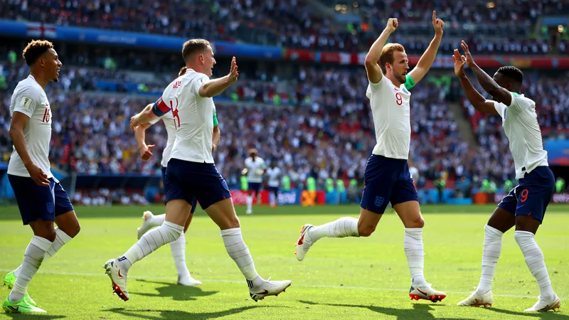 Pourquoi Kane est différent lors de cette Coupe du Monde — Football Harry Kane célébrant un but avec ses coéquipiers anglais lors d'un match de Coupe du Monde, portant le maillot blanc de l'Angleterre.
