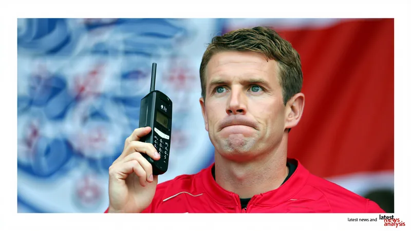 Un joueur de l'équipe d'Angleterre tenant un téléphone portable volumineux des années 1990, avec le maillot blanc et le logo de la FA