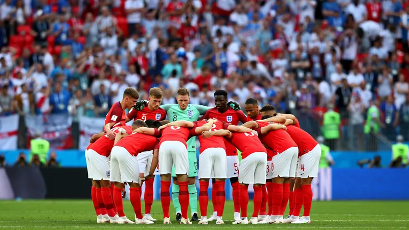Joueurs de l'équipe d'Angleterre en tenue blanche célébrant une victoire sur un terrain de football avec des supporters en arrière-plan.