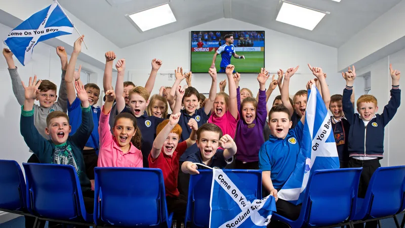 Retour aux sources pour John McGinn — Football World Cup News John McGinn souriant avec des enfants de l'école primaire St. Stephen's à Clydebank, portant des maillots de l'Écosse — latest news and analysis.