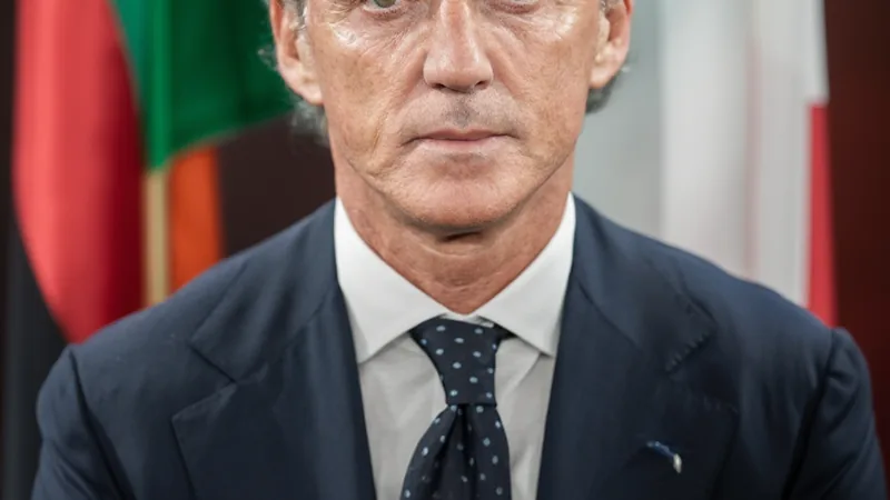 Roberto Mancini quitte Al Sadd et se rapproche de l'Italie — Football Roberto Mancini en costume, souriant, lors d'une conférence de presse avec le logo d'Al Sadd en arrière-plan. — latest news and analysis.