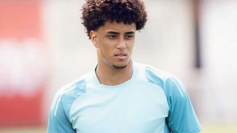 Un jeune joueur brésilien en tenue de Flamengo, souriant, avec le maillot rouge et noir, sur fond de terrain de football.
