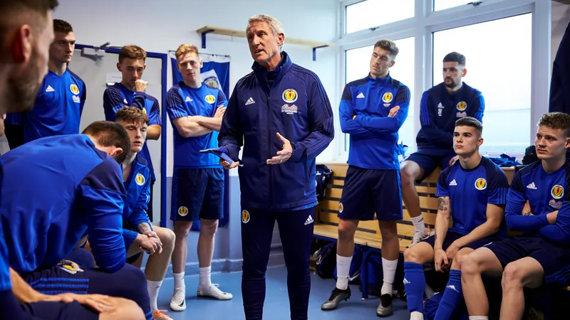 Steve Clarke en costume, debout dans un vestiaire, entouré de joueurs écossais en liesse après la qualification pour la Coupe du monde.