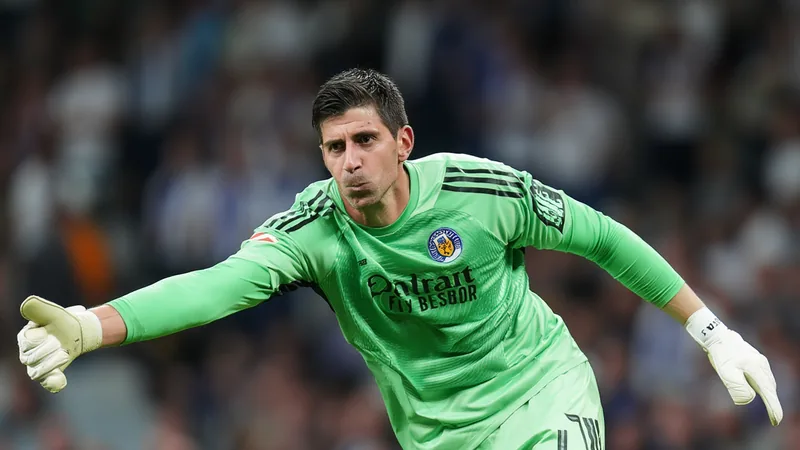 Thibaut Courtois en tenue du Real Madrid, souriant, dans le stade Santiago Bernabéu avec le logo du club en arrière-plan