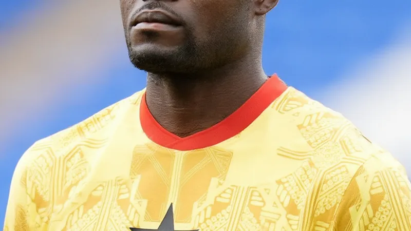 Thomas Partey privé d'entrée au Canada — Football World Cup News Thomas Partey en tenue d'Arsenal, regardant l'objectif, debout sur une pelouse de stade avec des supporters ghanéens en arrière-plan agitant des
