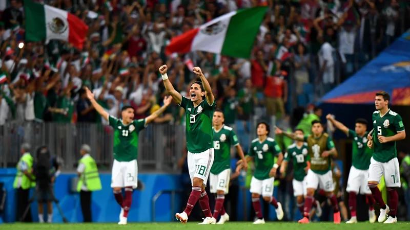 Mexique - Angleterre : tout savoir sur l'adversaire des 8es Joueurs mexicains célébrant une victoire sur le terrain, avec le drapeau du Mexique agité par les supporters en arrière-plan.