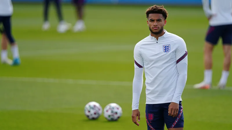 Reece James en tenue d'entraînement de l'Angleterre, souriant sur le terrain, avec le logo de la Coupe du monde en arrière-plan.
