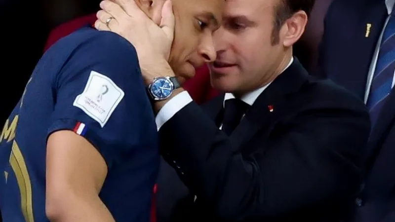 Macron salue Mbappé contre le racisme — Football World Cup News Kylian Mbappé en tenue de l'équipe de France, parlant lors d'une conférence de presse, avec le drapeau tricolore en arrière-plan.