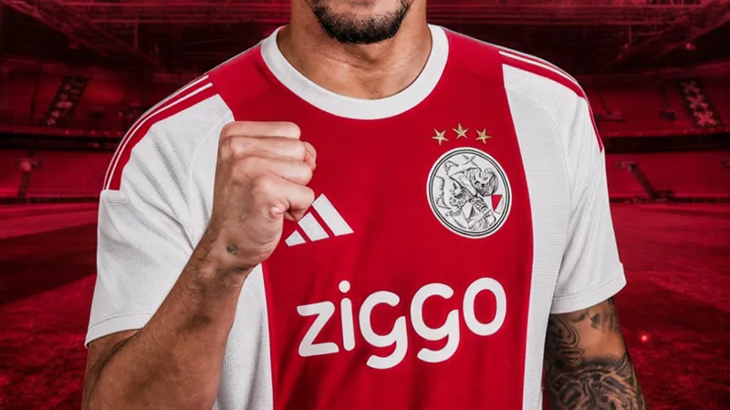 Un joueur de football brésilien en tenue de l'Ajax Amsterdam posant avec le maillot du club devant le stade Johan Cruyff.
