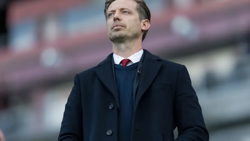 Michael Edwards quitte FSG — Football World Cup News Michael Edwards en costume-cravate, souriant, debout devant le logo du Liverpool FC à Anfield — latest news and analysis.