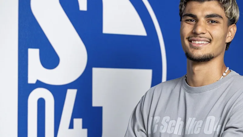 Mertcan Ayhan prolonge jusqu'en 2030 à Schalke 04 — Football World Jeune joueur de football en tenue de Schalke 04 posant avec un maillot et un stylo, souriant devant le logo du club — latest news and analysis.