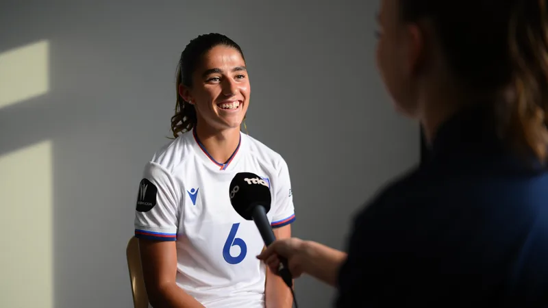 Alexia Putellas : « La Reina » passe au WSL — Football World Cup News Alexia Putellas souriante en tenue de London City Lionesses lors d'une conférence de presse, avec le logo du club en arrière-plan.