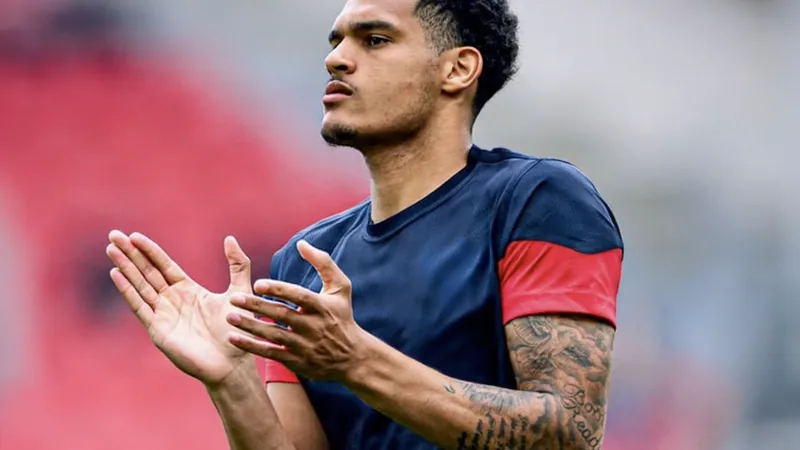 Jarell Quansah en action lors d'un match de Bundesliga avec le Bayer Leverkusen, portant le maillot rouge et noir, dans un stade plein.