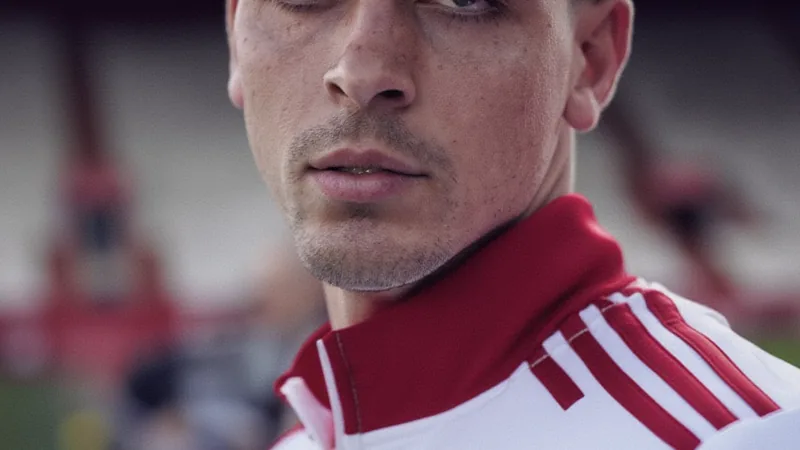 Juanlu Sánchez, joueur de Séville, en action sur le terrain, portant le maillot rouge et blanc, avec des supporters en arrière-plan.