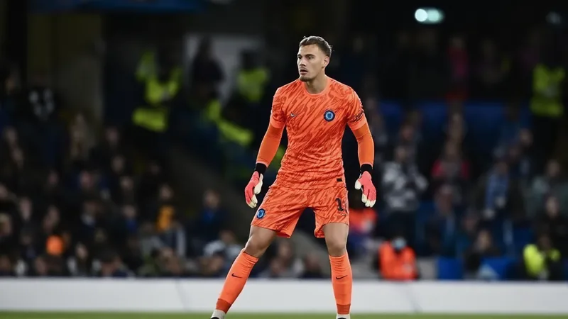 Filip Jorgensen prêté à Strasbourg — Football World Cup News Filip Jorgensen, gardien de but danois, en tenue de Chelsea, souriant lors d'un entraînement, avec le logo du RC Strasbourg en arrière-plan.