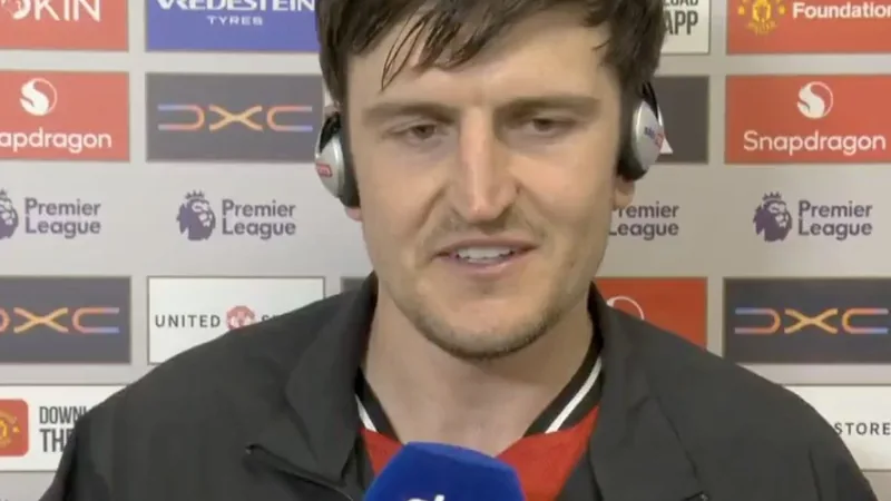 Harry Maguire en tenue d'entraînement de Manchester United, souriant, lors d'une conférence de presse, avec le logo du club en arrière-plan.