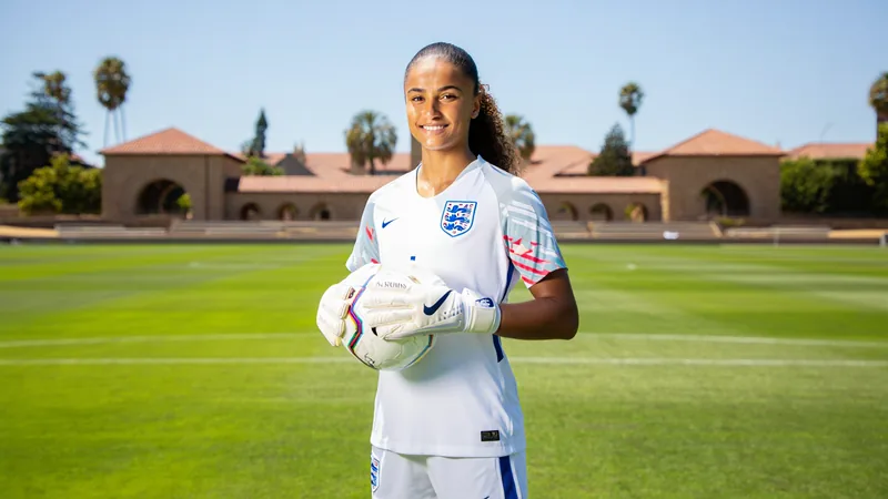 Jota : Coupe du monde, Stanford et mannequinat — Football World Cup Kaiya Jota, gardienne de but anglaise, en tenue de football, souriante, sur un terrain de Stanford avec des installations sportives en arrière-plan.