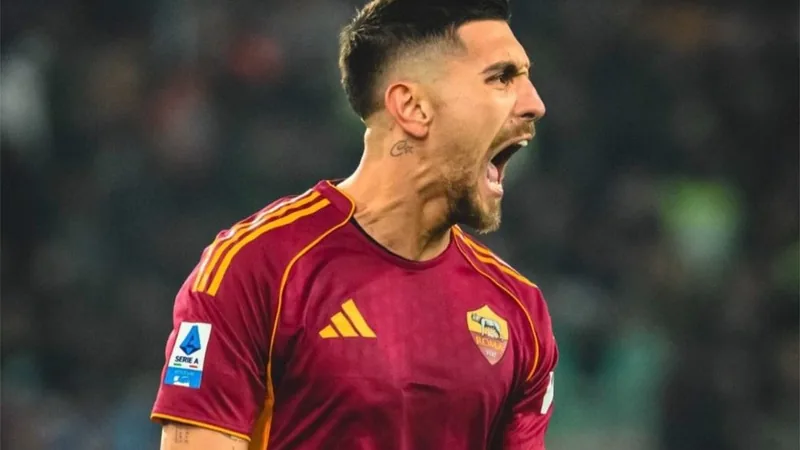 Lorenzo Pellegrini, capitaine de l'AS Roma, souriant en tenue de match sur la pelouse du Stadio Olimpico, avec le logo du club en arrière-plan.
