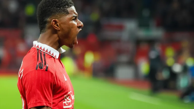 Marcus Rashford : avenir à Manchester United — Football World Cup News Marcus Rashford en tenue d'entraînement de Manchester United, souriant, sur le terrain du centre d'entraînement de Carrington, avec le logo du club