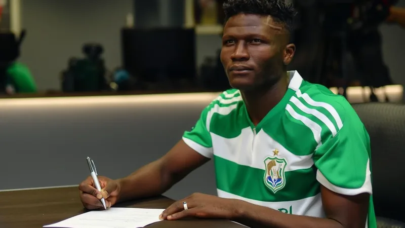 Al-Ahli fecha acordo com Abubakar Sidi Kinteh — Football World Cup Jovem futebolista Abubakar Sidi Kinteh vestindo a camisa do Al-Ahli, em campo de futebol, com bandeira da Arábia Saudita ao fundo.