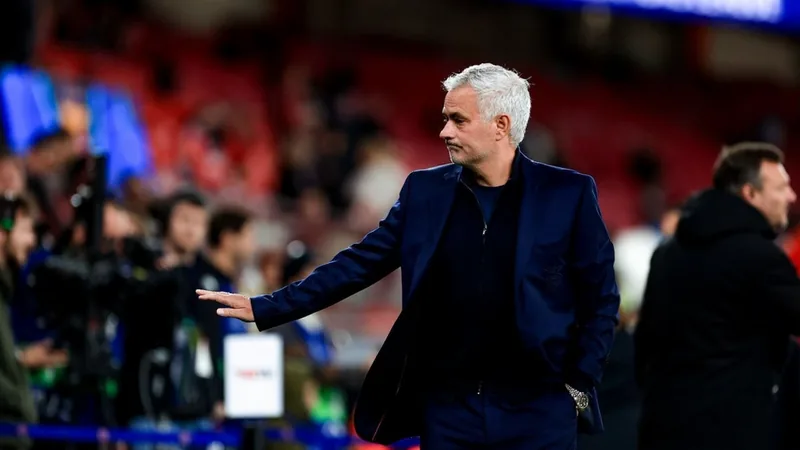 José Mourinho sorrindo durante entrevista, com microfone e fundo neutro, vestindo traje casual esportivo. — latest news and analysis.