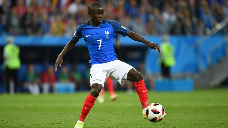 N'Golo Kanté sorrindo com a camisa da seleção francesa em um campo de treinamento, com outros jogadores ao fundo. — latest news and analysis.
