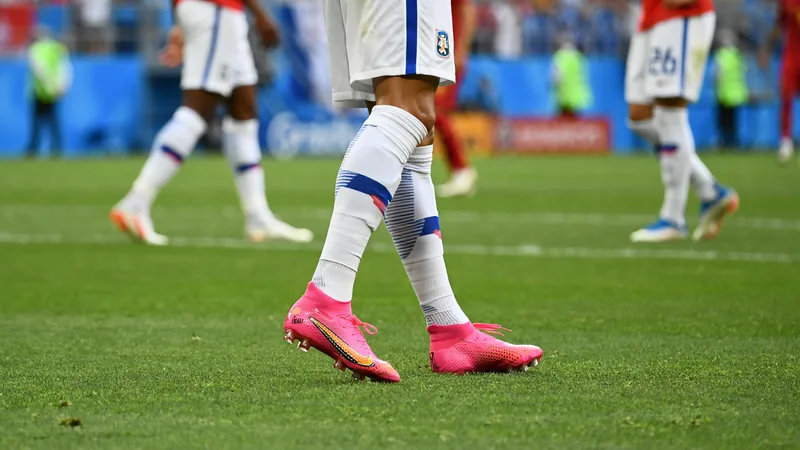 Jogador de futebol em campo usando chuteiras cor-de-rosa vibrante durante partida da Copa do Mundo de 2026, com gramado verde ao fundo.