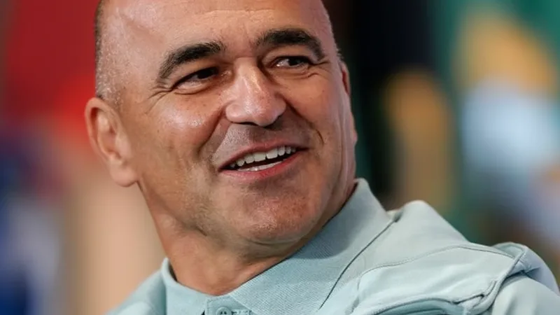 Roberto Martinez, selecionador de Portugal, a falar numa conferência de imprensa, com Cristiano Ronaldo ao fundo a treinar.