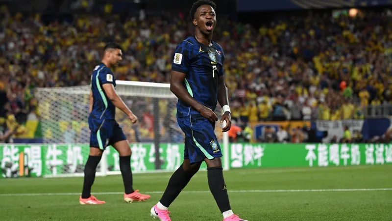 Vinícius Júnior com a camisa da seleção brasileira comemorando um gol, com a torcida ao fundo no estádio — latest news and analysis.