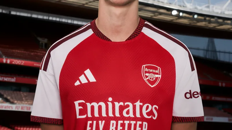 Arsenal fecha acordo para contratar jovem promessa Axel Donczew Jovem jogador Axel Donczew vestindo a camisa do Arsenal em um campo de treinamento, sorrindo e segurando uma bola de futebol.