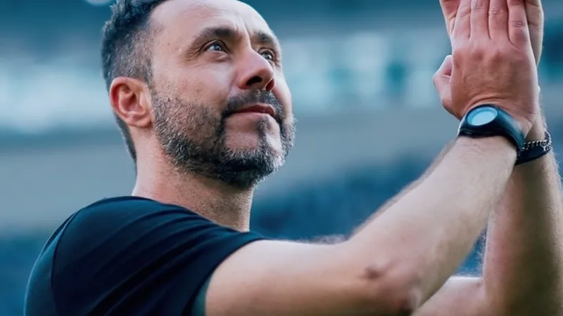 De Zerzi sobre Spence e Bergvall: 'Quem não quiser ficar, que saia' Roberto De Zerbi, técnico do Brighton, em entrevista coletiva, com expressão séria, falando ao microfone, com o logo do clube ao fundo.