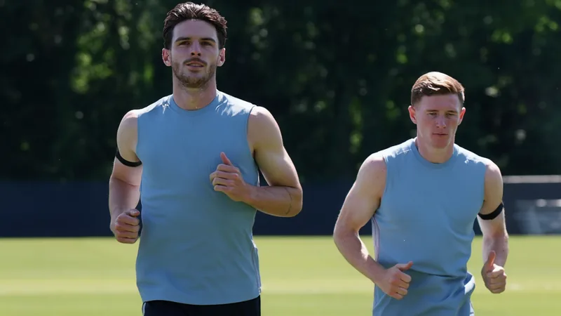 Declan Rice aconselha Elliot Anderson sobre pressão de taxas Declan Rice, do Arsenal, em campo durante uma partida, com expressão séria, usando uniforme vermelho e branco, sob luz do estádio.