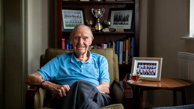 Ex-futebolista mais velho da Inglaterra elogia seleção na Copa Frank Blunstone, idoso de 91 anos, usando um cachecol da seleção inglesa, sorrindo em frente a um estádio de futebol. — latest news and analysis.