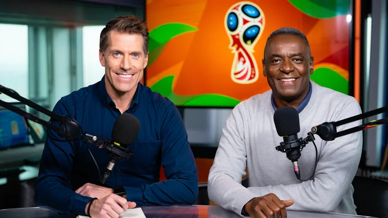 Os Melhores Momentos do Mundial — Football World Cup News Rick Edwards e Lloyd Griffith sorrindo em um estúdio de rádio, com um microfone e fones de ouvido, ao lado de uma bicicleta tandem decorada com