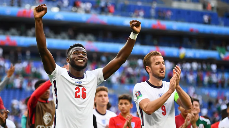 Inglaterra vence México no Azteca: 'Jogo icónico' — Football World Jogadores ingleses a celebrar no relvado do Estádio Azteca, com a multidão mexicana ao fundo e bandeiras da Inglaterra a ondear.