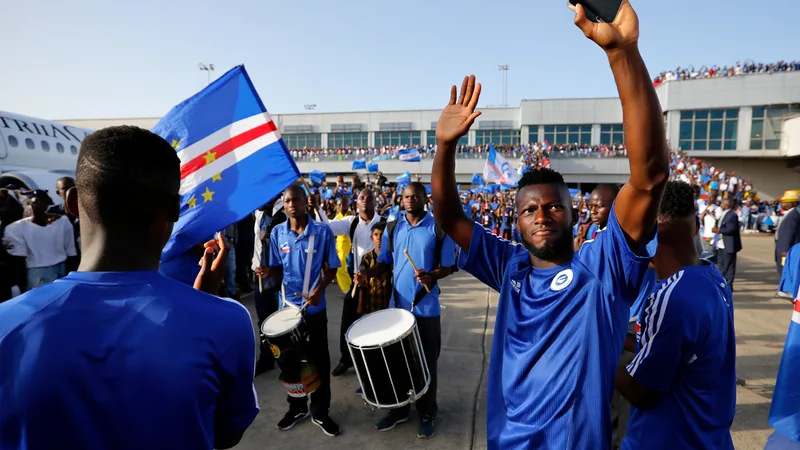 Multidão de adeptos vestidos com as cores de Cabo Verde acena bandeiras no Aeroporto Internacional Nelson Mandela, na Praia, enquanto os jogadores