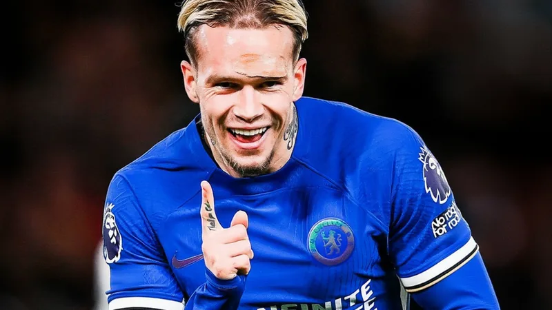 Mudryk tem suspensão anulada e está liberado — Football World Cup News Mykhaylo Mudryk, atacante ucraniano do Chelsea, comemora com o punho cerrado em campo, vestindo o uniforme azul do clube, com a torcida ao fundo.